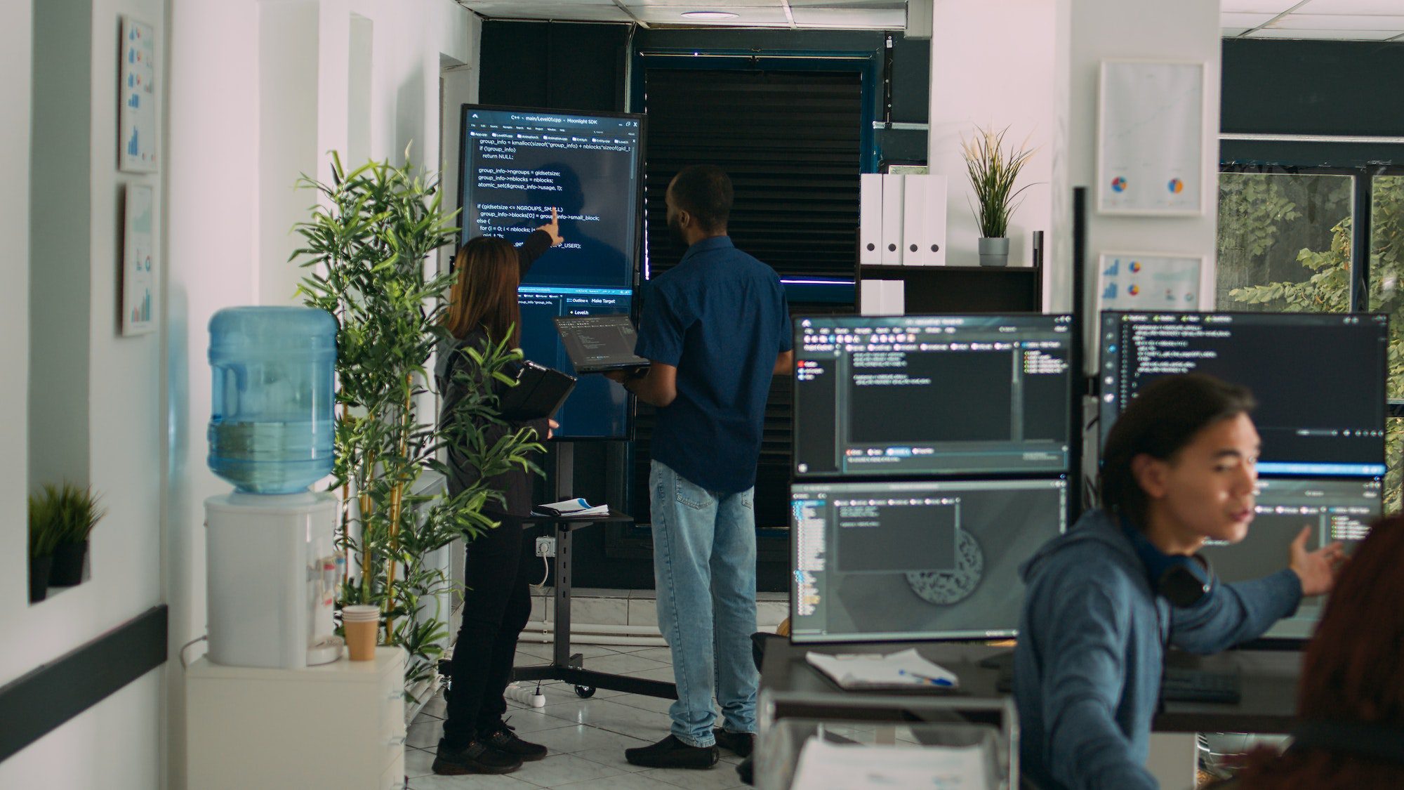 Diverse team of system developers analyzing code on big tv screen